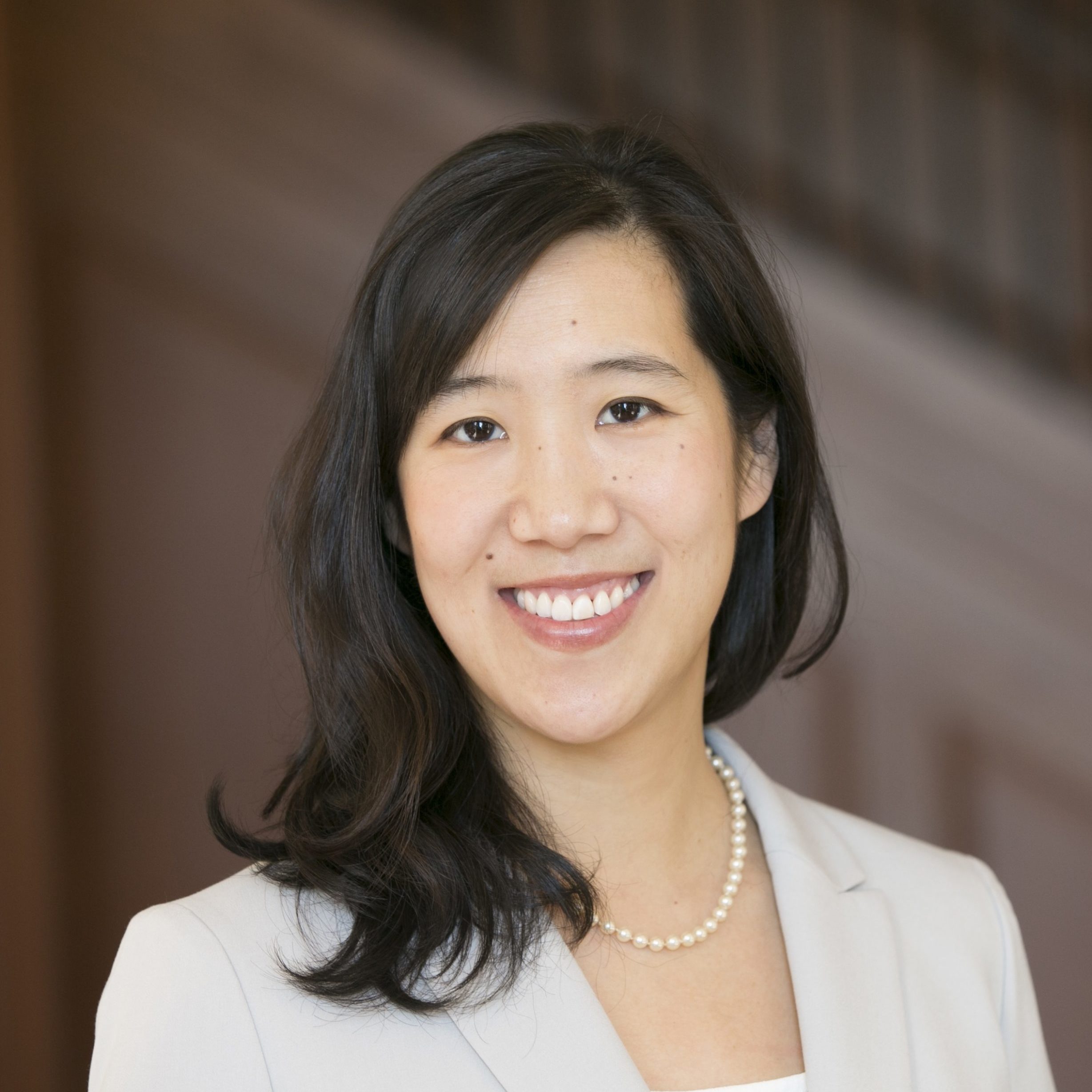 Headshot of Professor Laura Huang smiling and wearing a white blazer with a pearl necklace