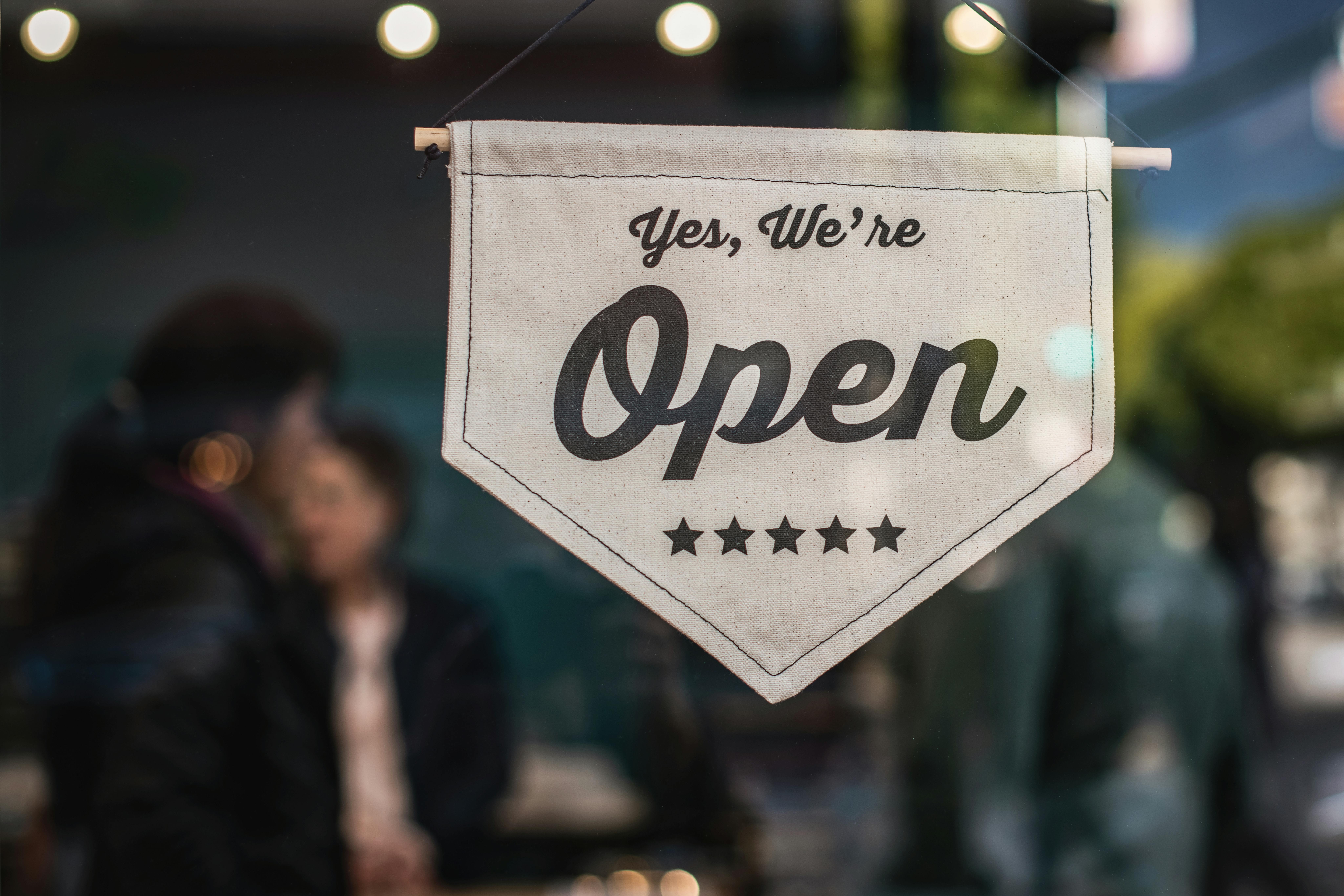 A "we are open" sign on a glass door with vibrant people in the background
