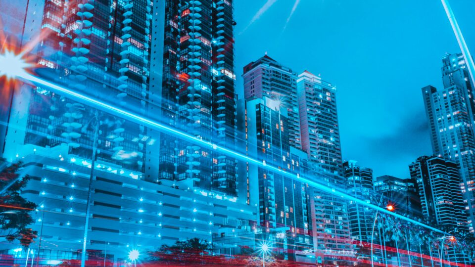 Buildings in a city that look futuristic with a blue dominant and red lights