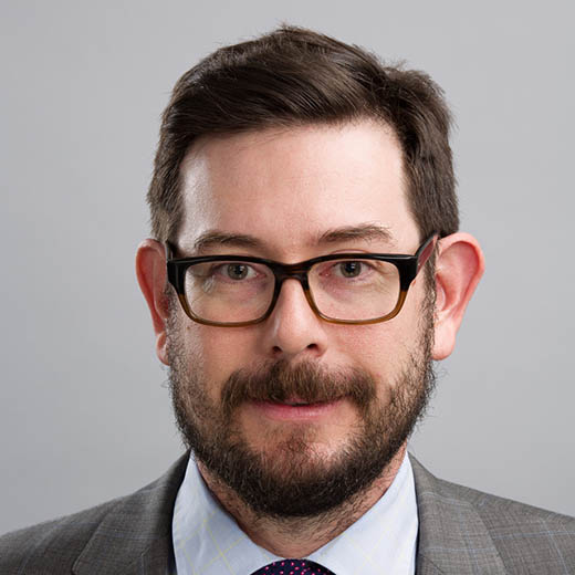 photo of a man with dark hair and a beard wearing glasses and a suit and tie