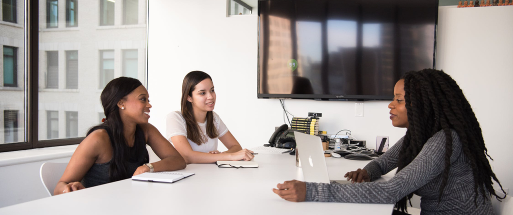women meeting at table with big monitor behind them