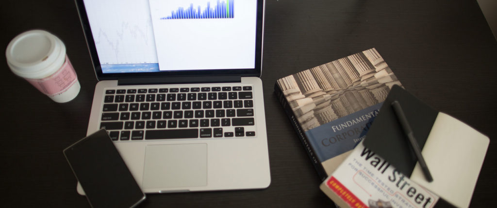 laptop with graph and wall street book