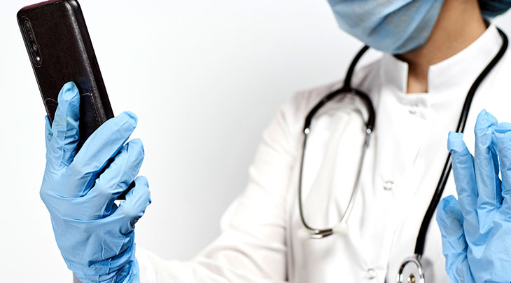 doctor wearing blue gloves and holding a cell phone