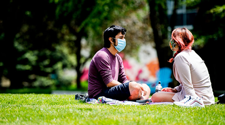 two students wearing face masks sitting on lawn