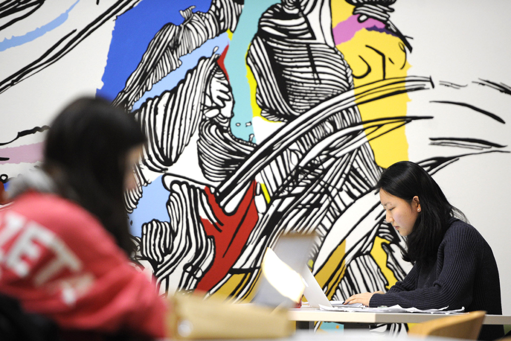 Photo of two woman sitting at separate tables doing work on their laptops
