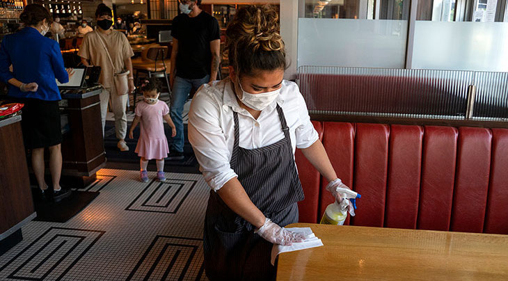 A frontline worker cleans a booth at a restaurant