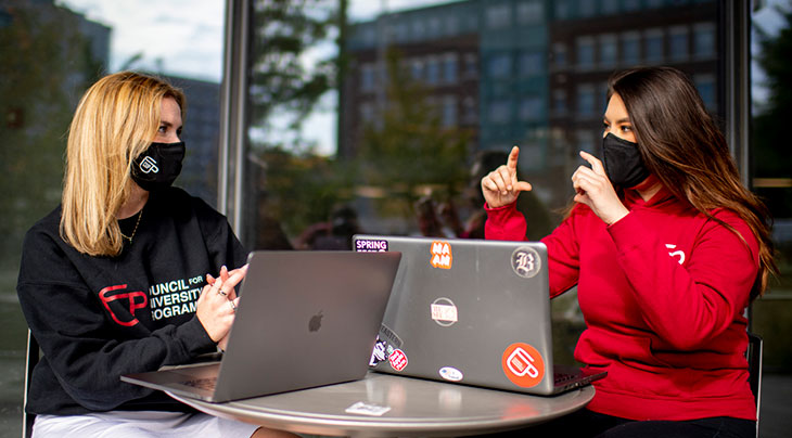 Photo of two students wearing masks and working at their laptops