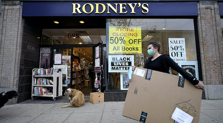 Photo of a passer-by carrying a box while walking past a bookstore that displays a store closing sign in its window