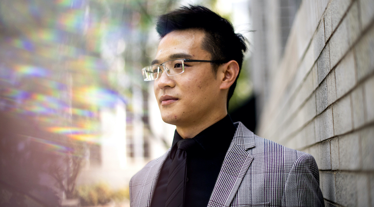 Portrait of Zhenyu Liao, a man with black hair and glasses wearing a blazer and black button up underneath