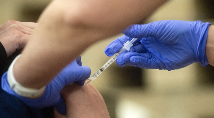 Photograph of a medical professional wearing gloves administering a vaccine into an arm