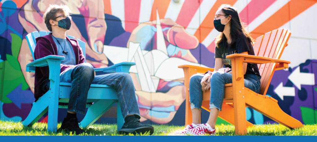 Two Northeastern students sitting in adirondack chairs with masks on