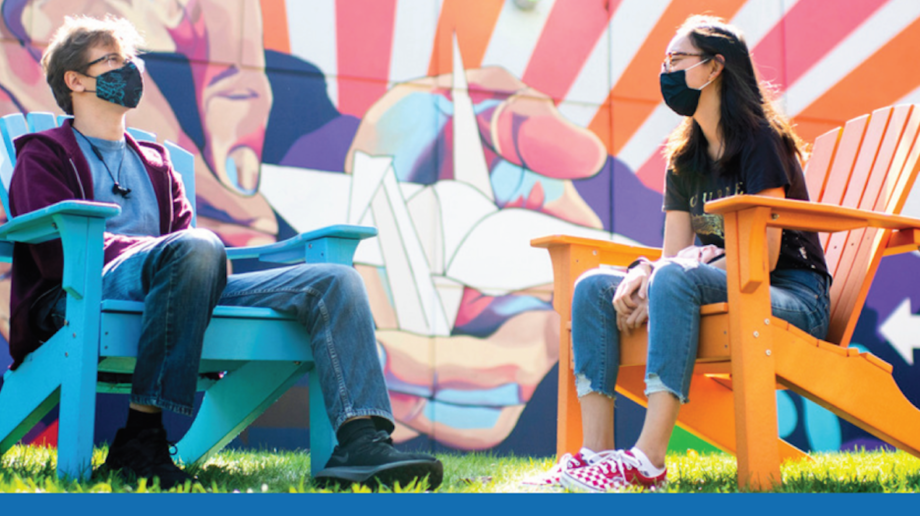 Two Northeastern students sitting in adirondack chairs with masks on