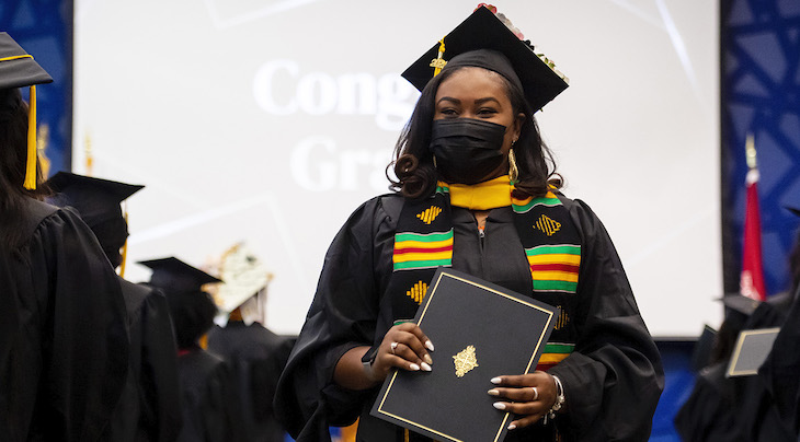 photo of a student holding her diploma wearing a cap and gown