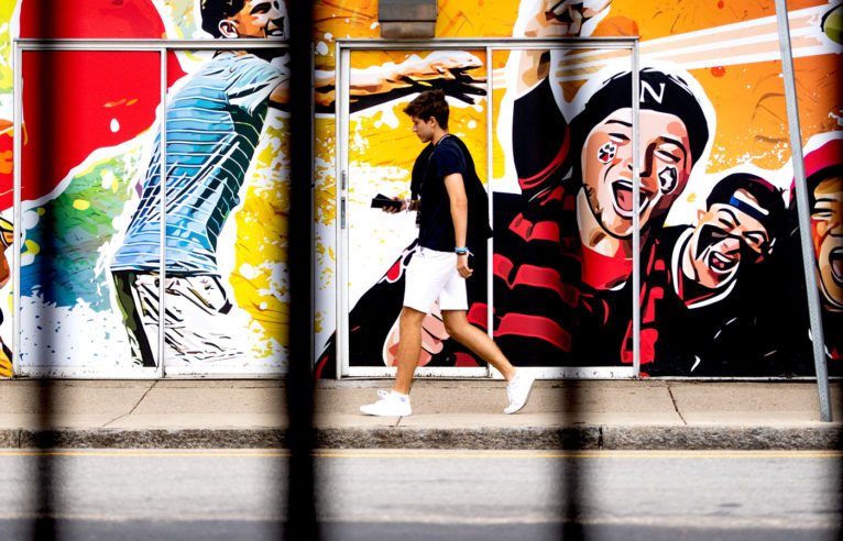 photo of a student walking along the sidewalk in front of a mural