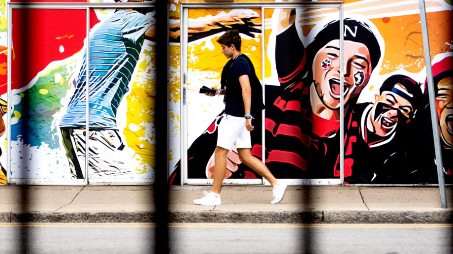 photo of a student walking along the sidewalk in front of a mural