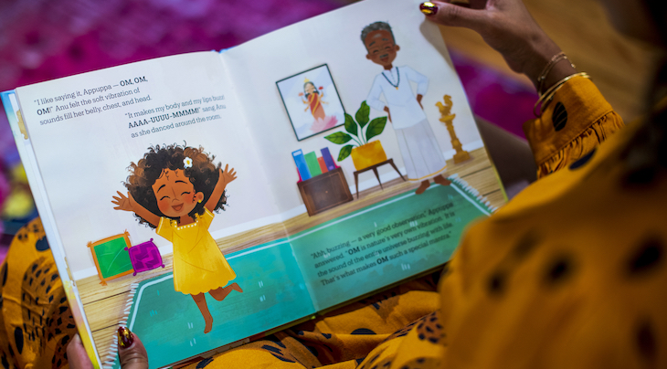 Photo of a woman reading a book which features an illustration of a young girl dancing in a yellow dress