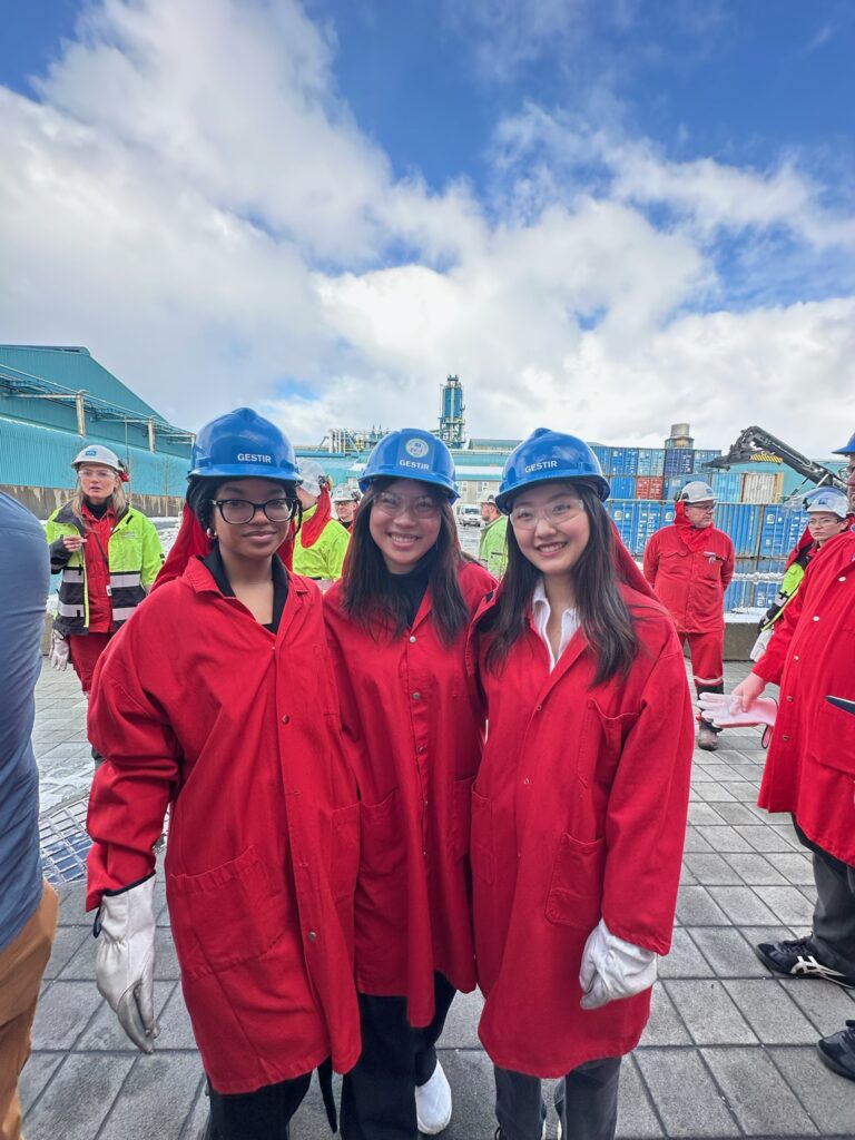 Three students in red lab coats and blue hard hats